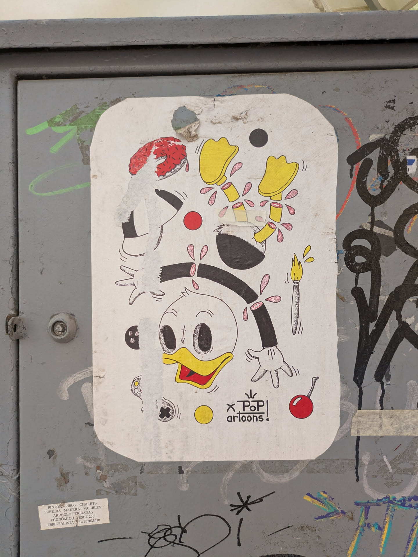 A white rectangular sticker, peeling in places, featuring a surreal illustration of Donald Duck by Pop! Cartoons. Donald's head is near the bottom center, with his iconic yellow beak and sailor cap replaced by a red sprinkled donut. His feet are floating at the top. A dismembered hand and a paintbrush complete the design. The sticker is adhered to a grey metal surface covered in additional graffiti. Text reads 'x Pop! artoons!'