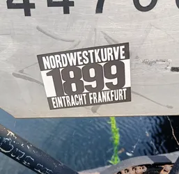 A black and white sticker with the text Nordwestkurve 1899 Eintracht Frankfurt.  The sticker is attached to a metallic surface.