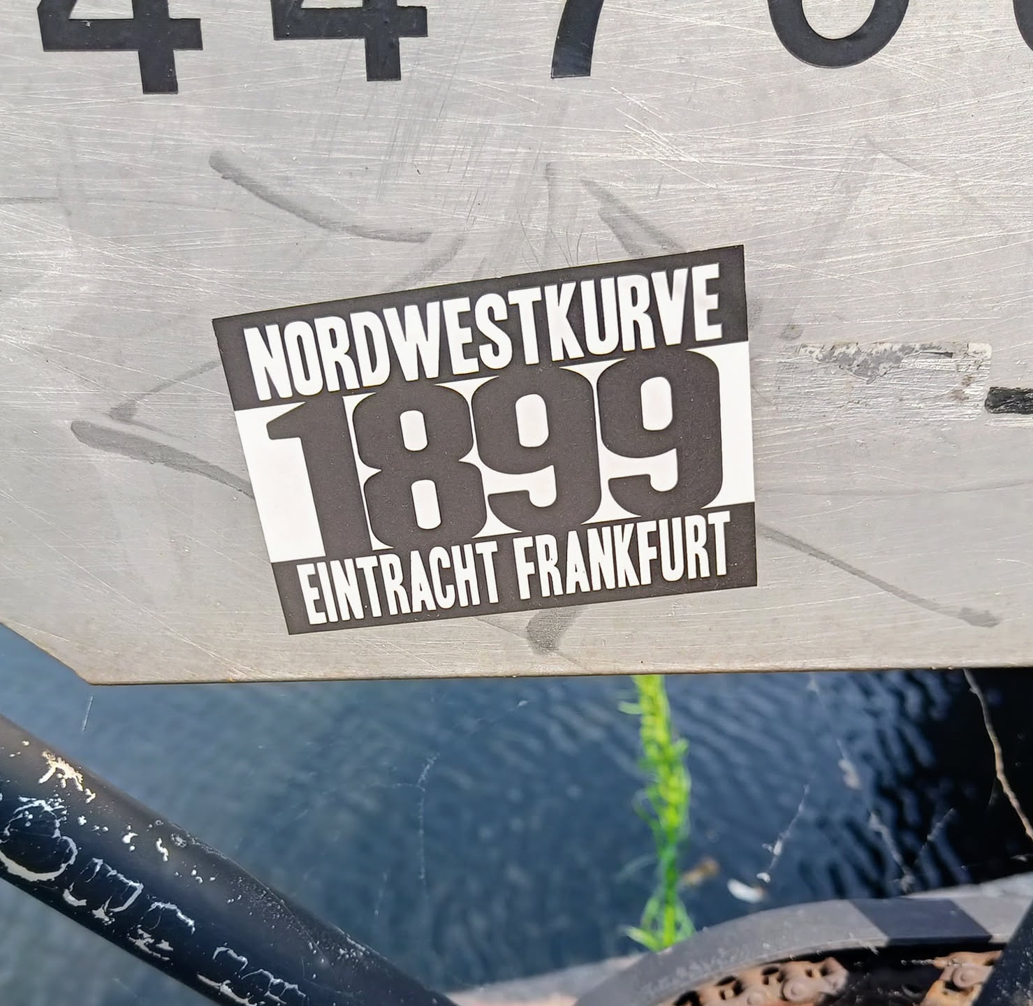 A black and white sticker with the text Nordwestkurve 1899 Eintracht Frankfurt.  The sticker is attached to a metallic surface.