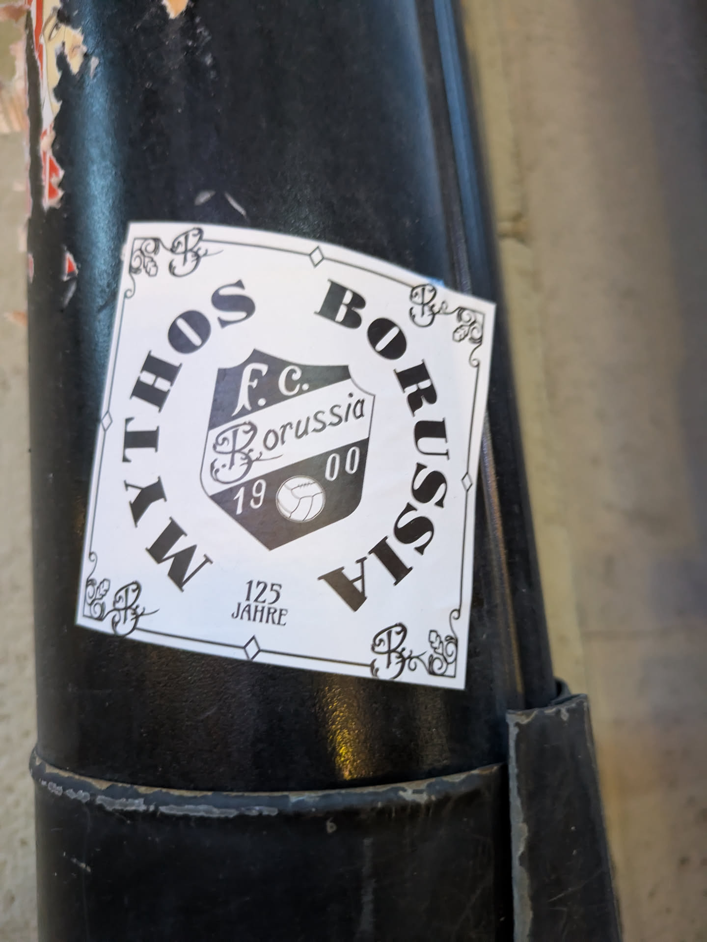 A white, rectangular sticker with a black border. In the center is a shield-like emblem in black and white, containing the text 'F.c. Borussia', the year '1900', and a stylized soccer ball. The words 'MYTHOS' are curved along the top left of the sticker and 'BORUSSIA' along the top right, with '125 JAHRE' (125 Years) below the emblem. Decorative flourishes are present in the corners and around the text.
