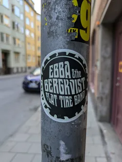 A round black and white sticker with the band's name, Ebba & the Bergkvist Flat Tire Band, in a stylized font. The design resembles a circular saw blade.
