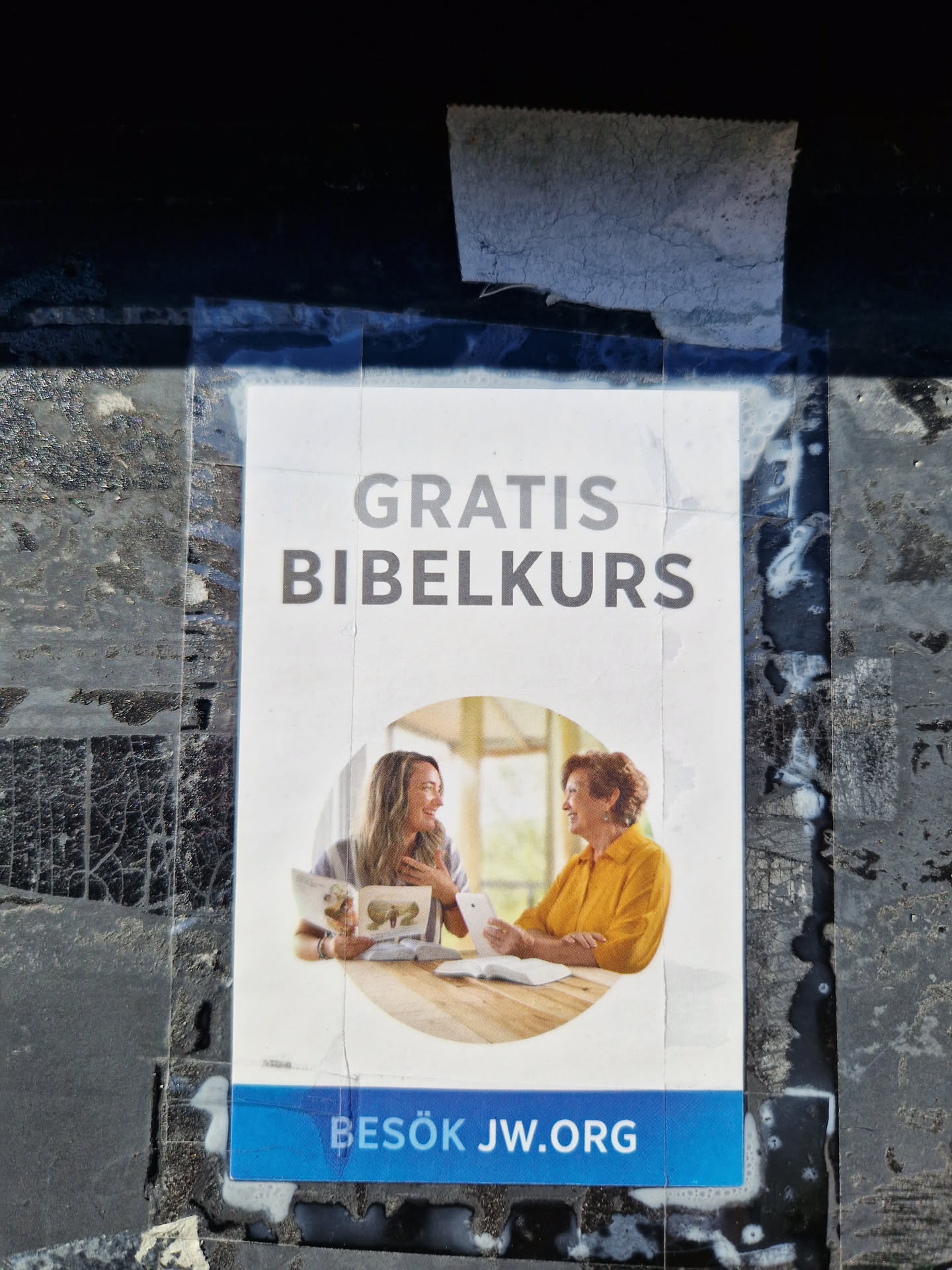 A sticker advertising a free Bible course.  It features an image of two women studying the Bible together and includes a website address.  The text on the sticker is in Swedish.