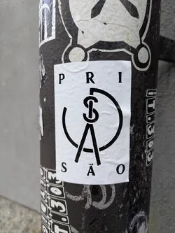 Black and white sticker with the word PRISÃO (Prison in Portuguese) forming a circle around a symbol that looks like a compass or a pair of dividers. The style is minimalist and geometric.