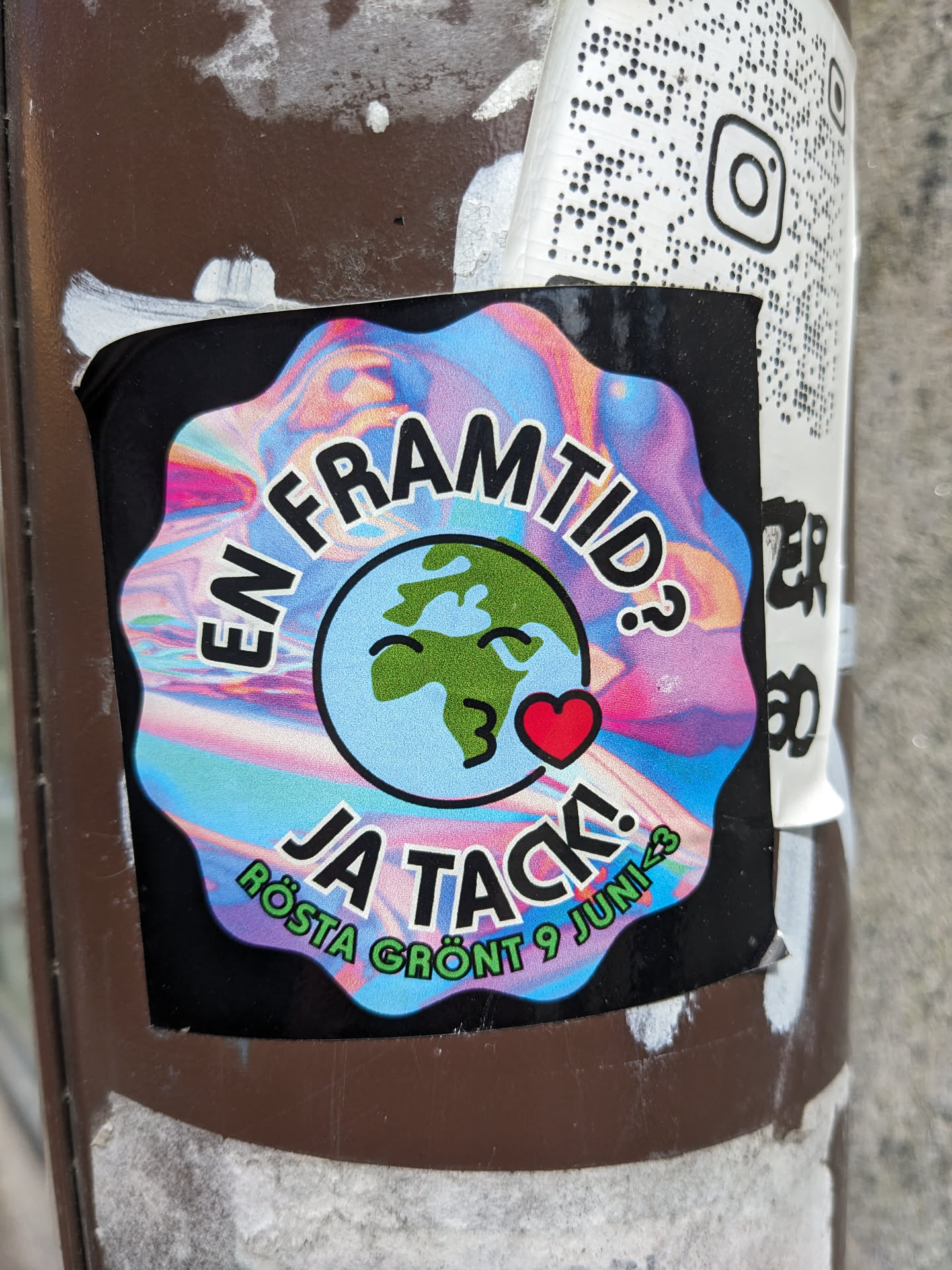 A sticker with a colorful design featuring a cartoon Earth blowing a kiss. The text on the sticker says: "En framtid? Ja tack! Rösta grönt 9 Juni", which translates to "A future? Yes, thank you! Vote green June 9th".