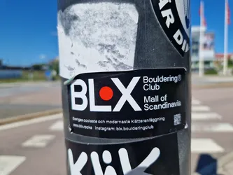A black and white sticker with a red dot and the text BLX. It also says Bouldering Club Mall of Scandinavia.  There is a QR code and social media links included.