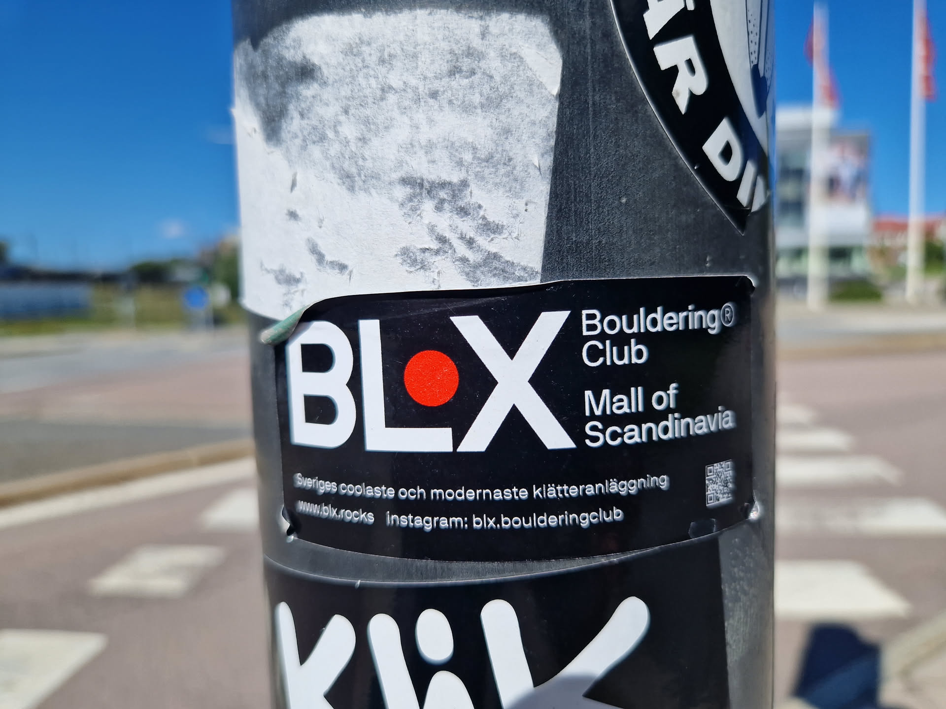 A black and white sticker with a red dot and the text BLX. It also says Bouldering Club Mall of Scandinavia.  There is a QR code and social media links included.