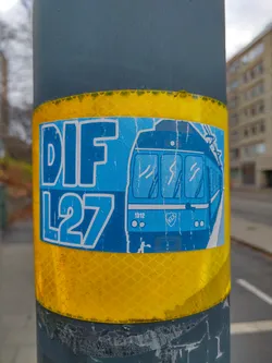 A blue and white sticker featuring the text "DIF L27" and an illustration of a tram. The sticker is affixed to a yellow reflective band on a gray pole.