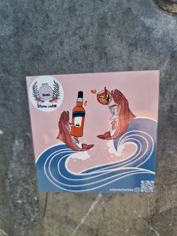 A sticker featuring two salmon toasting with an Aperol Spritz in the middle of an ocean wave. It has a minimalist design with a pink background and blue waves. There is a small logo in the top left corner. The sticker also includes a QR code linking to the artist's Instagram.