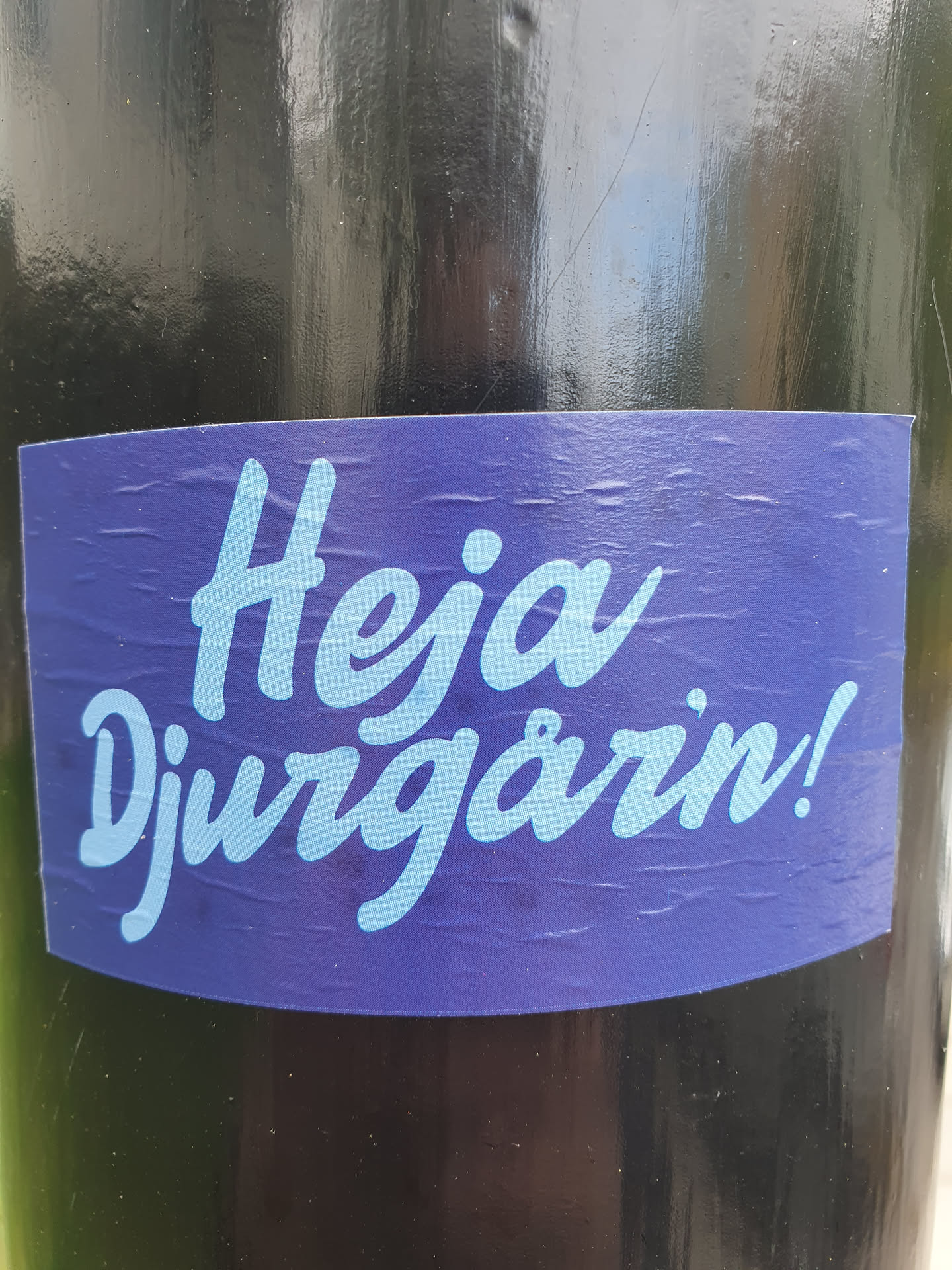 A purple sticker with the text "Hej Djurgården!" in light blue. The sticker is placed on a dark surface.