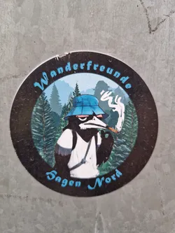 Round sticker featuring an illustration of an anthropomorphic bird wearing a bucket hat, smoking a cigarette, and carrying a backpack in a forest landscape. The text "Wanderfreunde Sagen Nord" is written around the illustration.