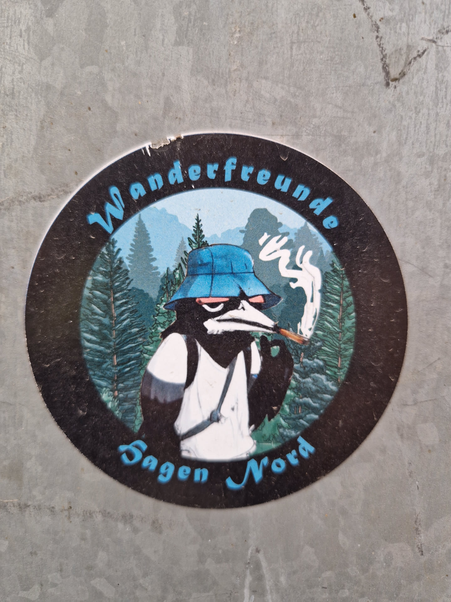 Round sticker featuring an illustration of an anthropomorphic bird wearing a bucket hat, smoking a cigarette, and carrying a backpack in a forest landscape. The text "Wanderfreunde Sagen Nord" is written around the illustration.