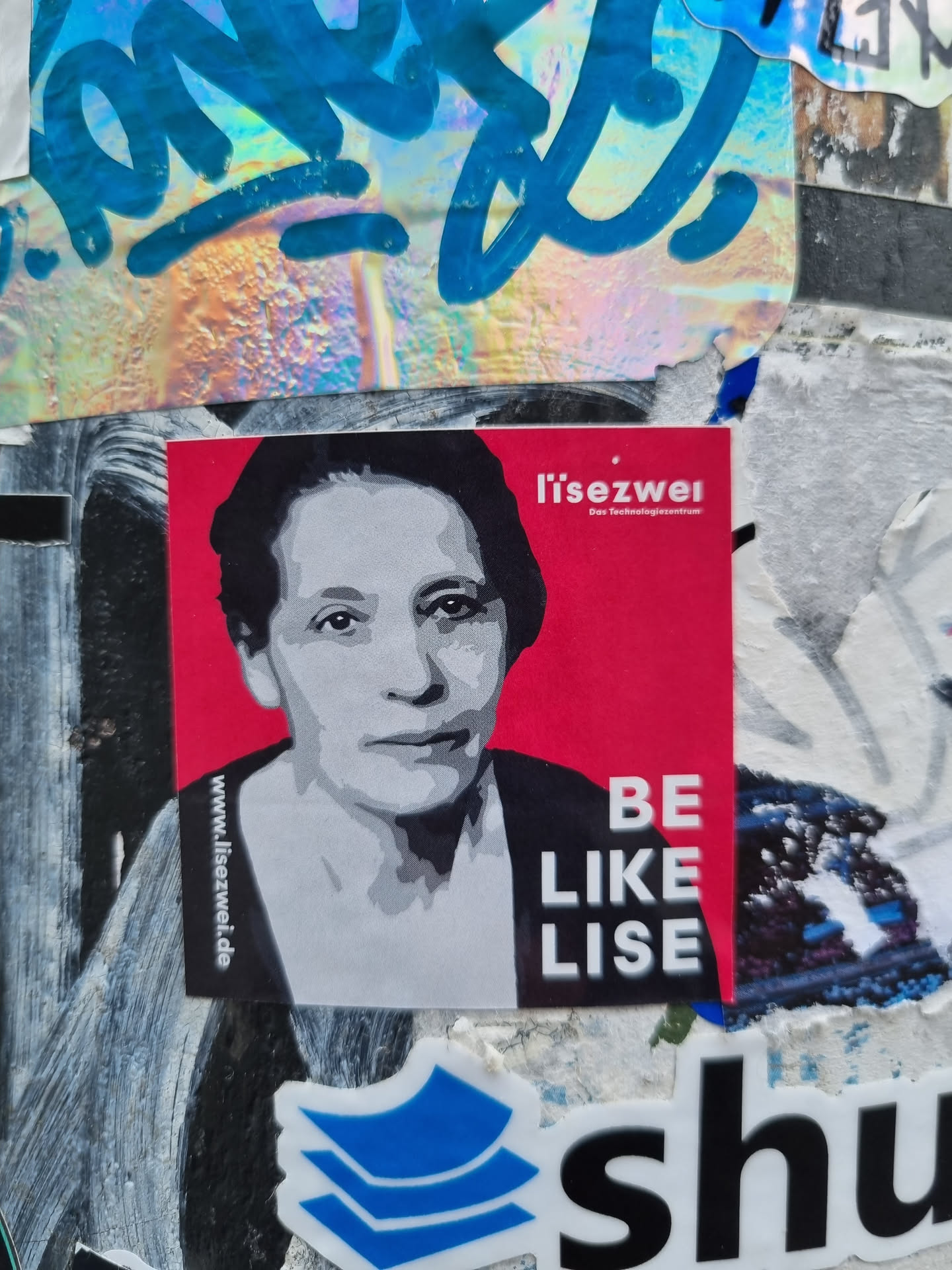 A sticker featuring Lise Meitner, a prominent physicist. The sticker has a red background with a black and white portrait of Meitner and the text "Lise Meitner - Be like Lise".  The website www.lise-meitner.de is visible at the bottom.