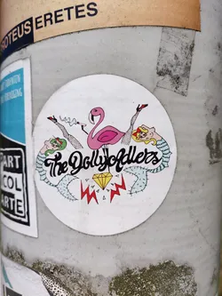 Round sticker with an illustration of a flamingo in the center, with two pairs of legs and high heels on either side. The text 'The DollyOdders' is written in a stylized font above a diamond. The style is reminiscent of vintage pin-up art with a touch of surrealism.