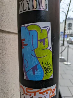 This sticker features a unique design with blue and green colors, accented with purple and red. It's a hand-drawn graffiti style artwork.