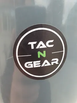 A round sticker with Tac N Gear written in a circle. The text is in white with a green N. The background is black, and it has a white border.
