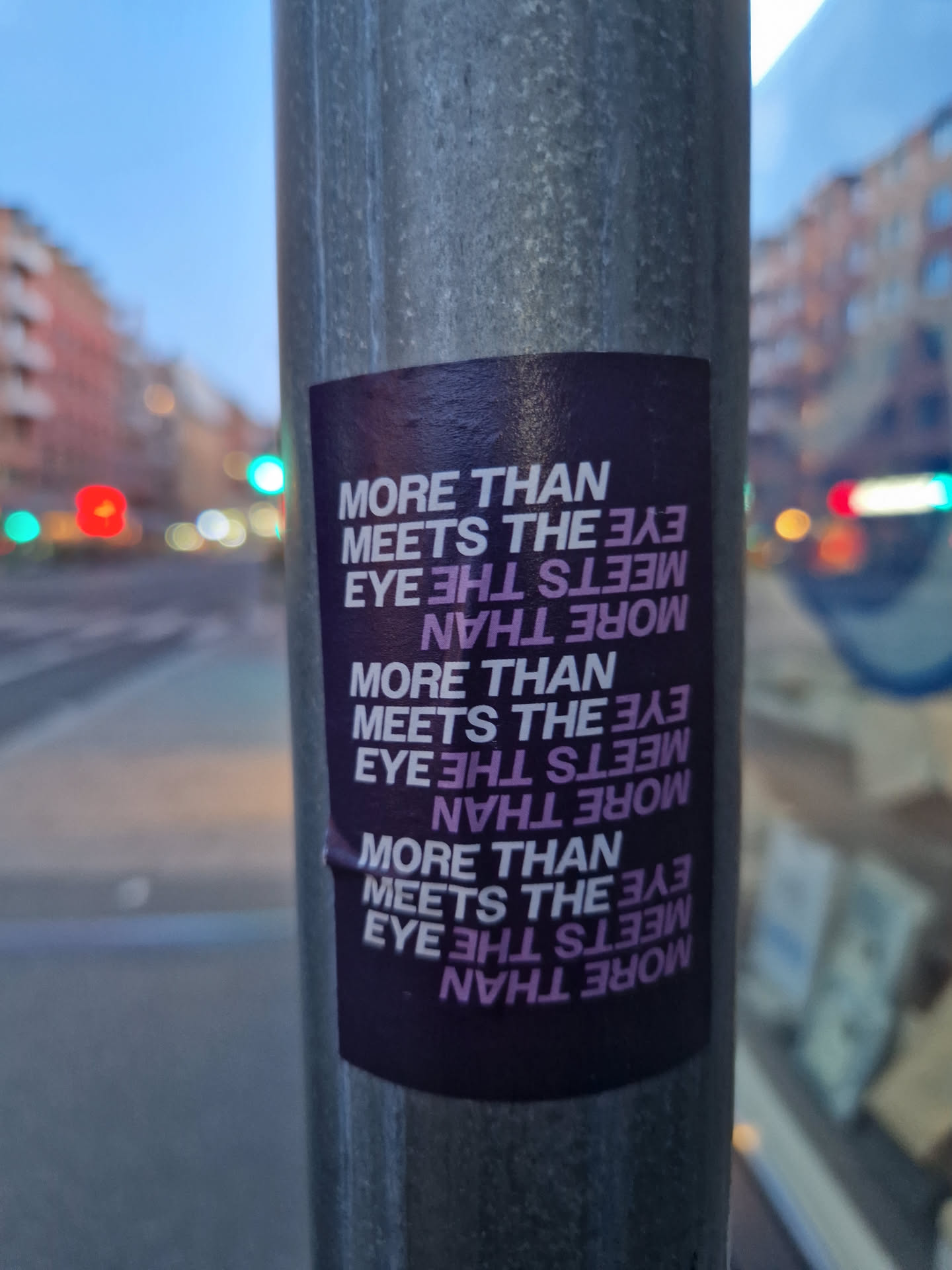 A sticker on a pole with the text 'More than meets the eye' repeated multiple times in a mirrored pattern. The sticker is dark purple with light purple text.