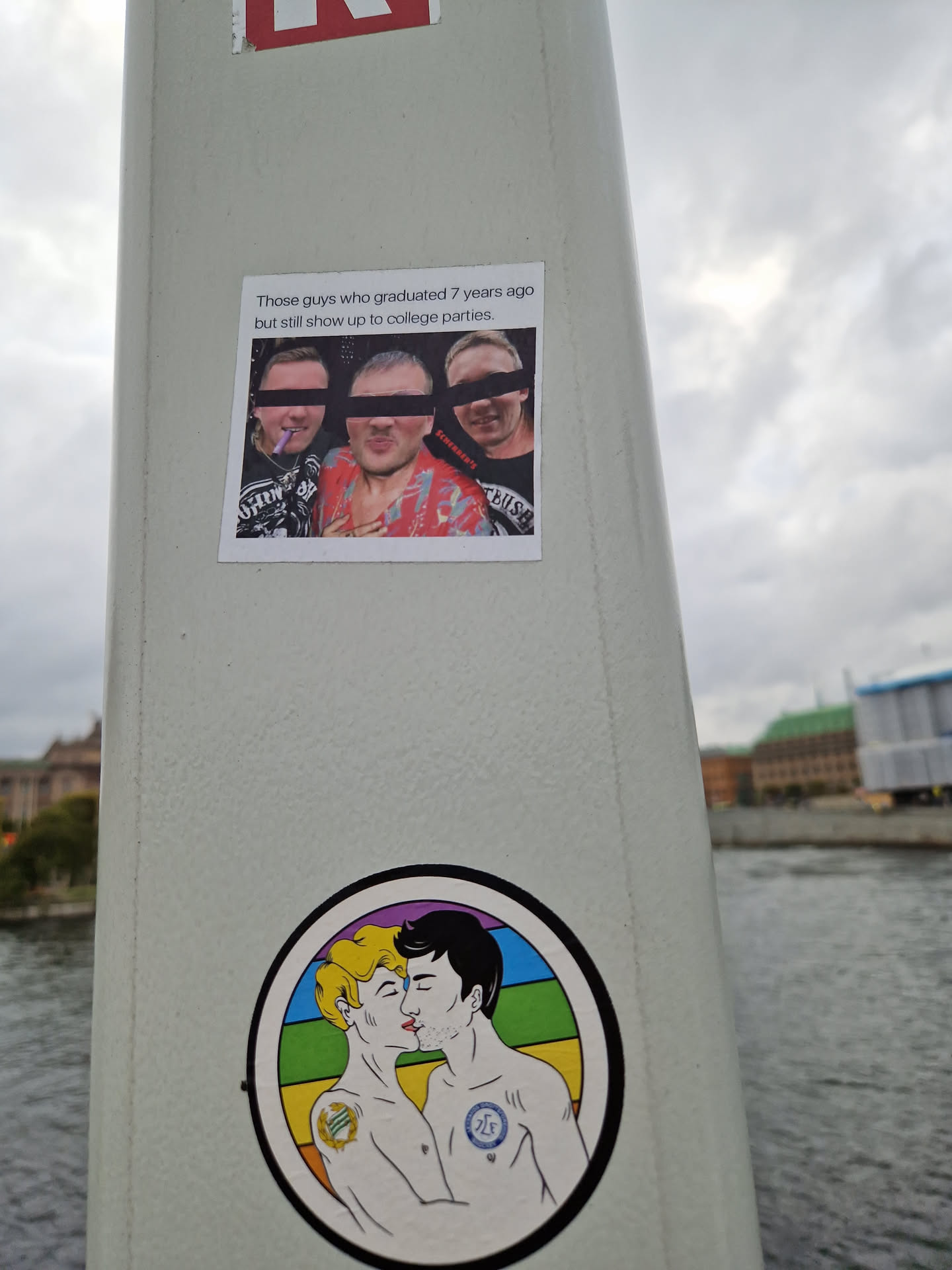 A sticker featuring a drawing of two men kissing, set against a rainbow background.  Another sticker above it shows a photo of three men, likely at a party. 