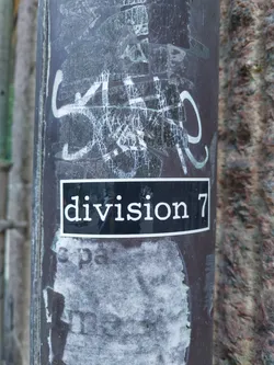 A black and white sticker with the text "division 7" on a dark background attached to a pole.