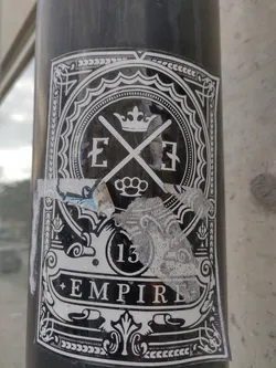 Black and white sticker with intricate design. It features a crown, crossed letter E's, a number 13, and the word Empire. The style is ornate and slightly gothic.