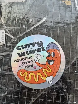 Holographic sticker of a cartoon currywurst wearing a beanie. The text on the sticker says "Curry Wurst" and "coucher avec moi" which translates from French to "sleep with me".