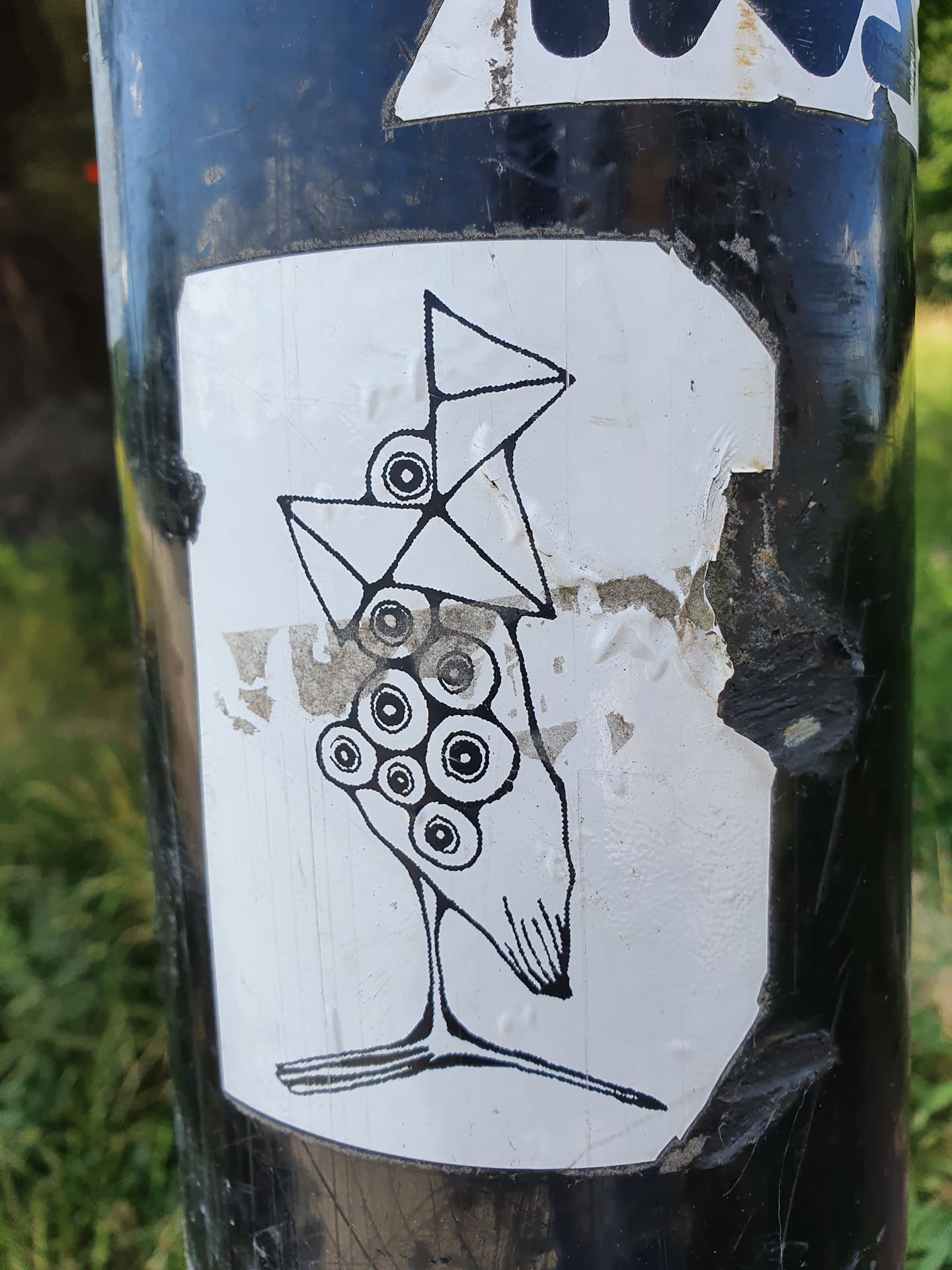 Black and white illustration of a bird with geometric shapes. The bird has a triangular head and body, with circular eyes. It has a long, thin neck and legs. The sticker is on a black pole.