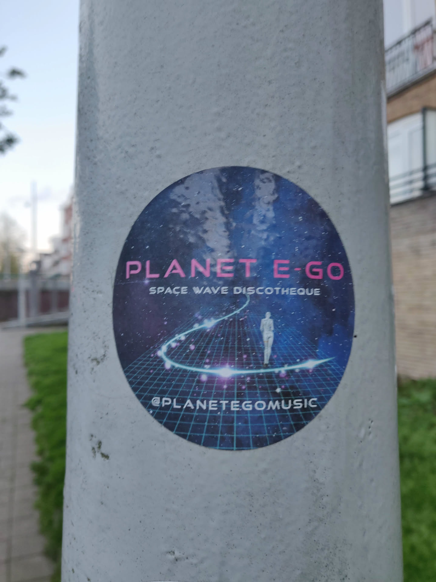 Round sticker featuring a cosmic design, a person walking on a glowing path, and grid-like background.  Text includes 'PLANET E-GO' and 'SPACE WAVE DISCOTHEQUE'. A social media handle is visible at the bottom.
