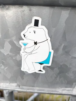 A sticker featuring a stylish polar bear wearing a top hat and bow tie, sitting on a teal chair and holding a martini glass. The illustration is minimalist and elegant.