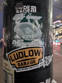 A sticker for Ludlow Garage in Cincinnati, OH.  The sticker features their logo, the text 'Where Live Music Comes to Play', and a smaller sticker underneath featuring a stadium illustration and German text. The smaller sticker has  'Für immer Weserstadion' which translates to 'Forever Weserstadion'. There is also a logo that says De Saus.