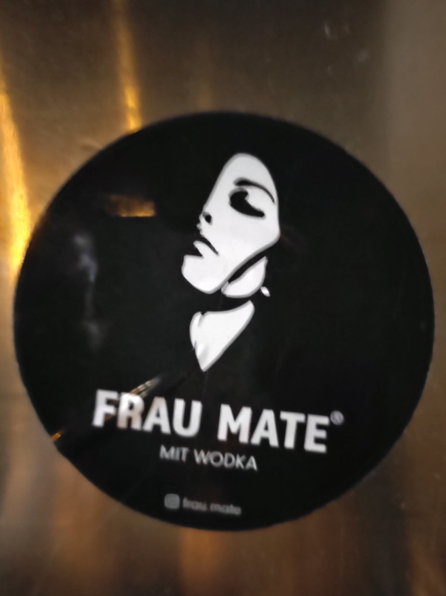 Black and white round sticker featuring a stylized female face and the text "FRAU MATE® MIT VODKA".  A small Instagram logo and handle are visible at the bottom.