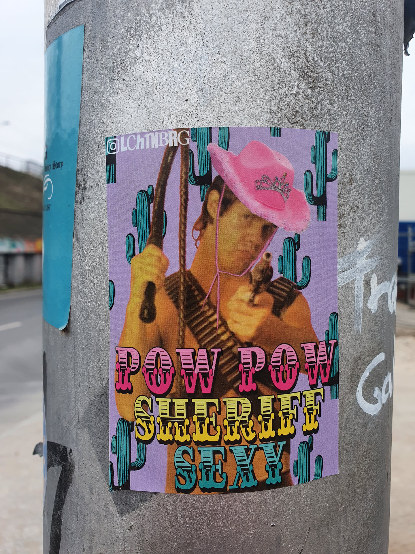 A sticker featuring a man in a pink cowboy hat, holding a whip and a gun. The background is purple with cacti. The text 'Pow Pow Sheriff Sexy' is prominently displayed.