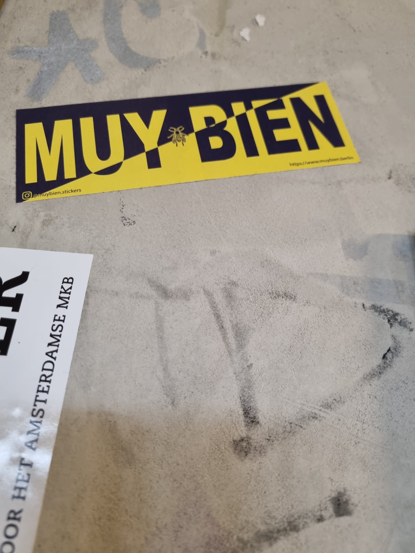 A yellow and dark blue sticker with the words "MUY BIEN" (Spanish for "Very Good") in a bold sans-serif font. A small bee illustration separates the words. The sticker includes a social media handle (@muybienstickers) and a website URL (https://www.muybienstickers.com).