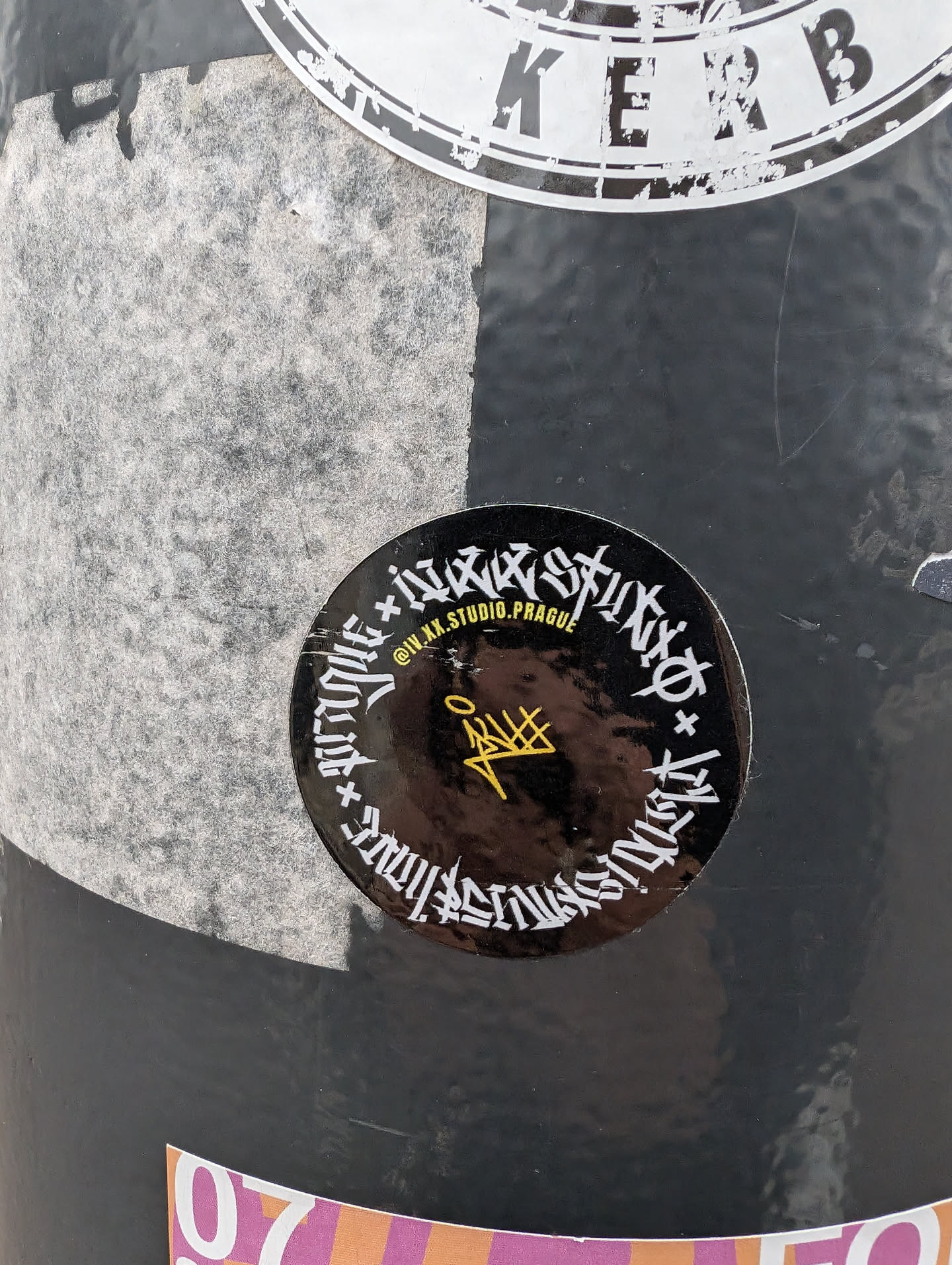 A round sticker with a black background and gold lettering. The text is stylized and difficult to fully decipher but appears to include the Instagram handle @IVAX.STUDIO.PRAGUE.  A small, stylized symbol is in the center.