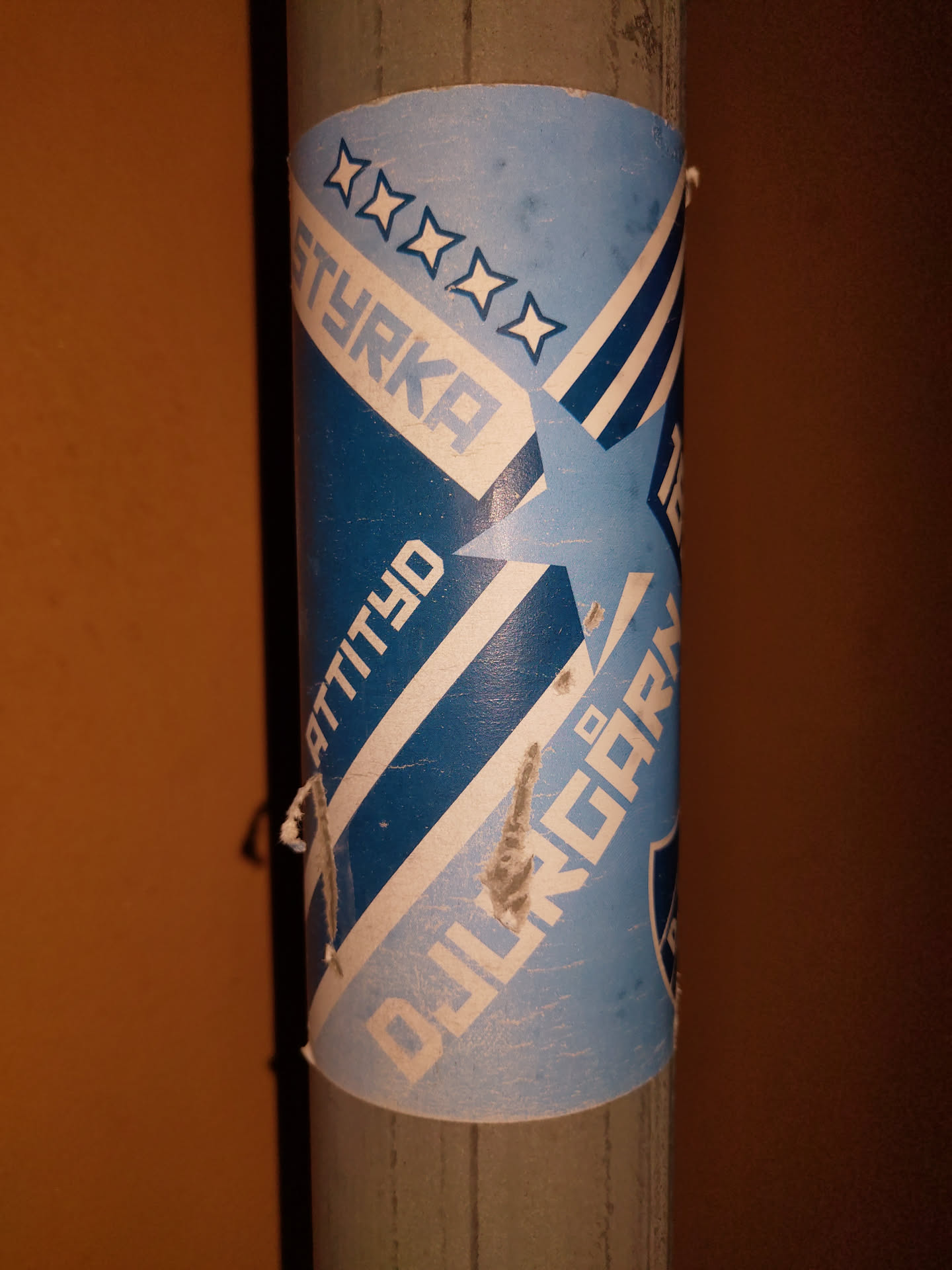A blue and white sticker with a star design. Text on the sticker reads "Styrka", "Attityd", and what looks like "Djur". There are four stars at the top and a larger star incorporated into the design.  The sticker shows some signs of wear.