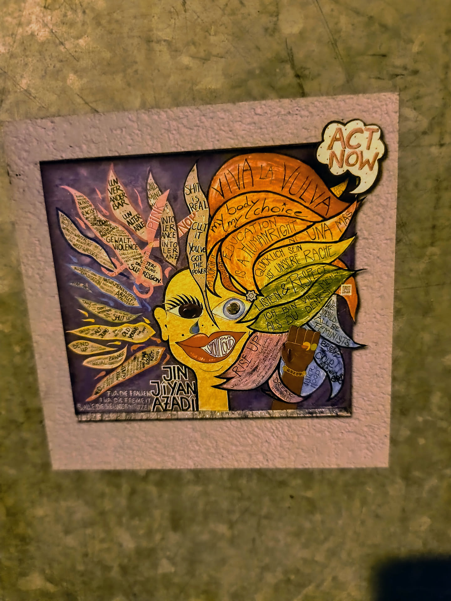 This sticker features a mixed-media portrait with half of the face in yellow tones and the other in purples and blues. The artwork includes empowering phrases like "Viva la Vulva," "my body my choice," and "Education is a human right" integrated into the design. A speech bubble says "Act Now!", emphasizing the call to action. The image is framed with a textured, pink-colored border, giving it a crafted, artistic feel.
