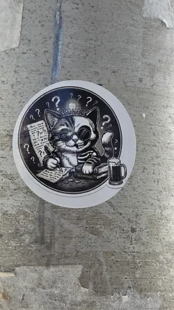 Street sticker A circular monochrome sticker with a white border featuring a depiction of Schrödinger's cat. The cat is split vertically down the middle: its left side is alive and furry, wearing round spectacles and writing on paper, while its right side is a skeleton with an exposed skull and ribcage. Floating question marks surround its head alongside a glowing light bulb. On the desk in front of the cat are papers with question marks, scattered coins, a stack of books with one reading 'Schrödinger' on the spine, and a full mug of beer on the right edge.