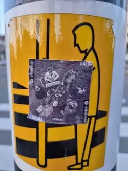 A black and white photo sticker of a band called DynamOs. The sticker is on a yellow sign with a pictogram.