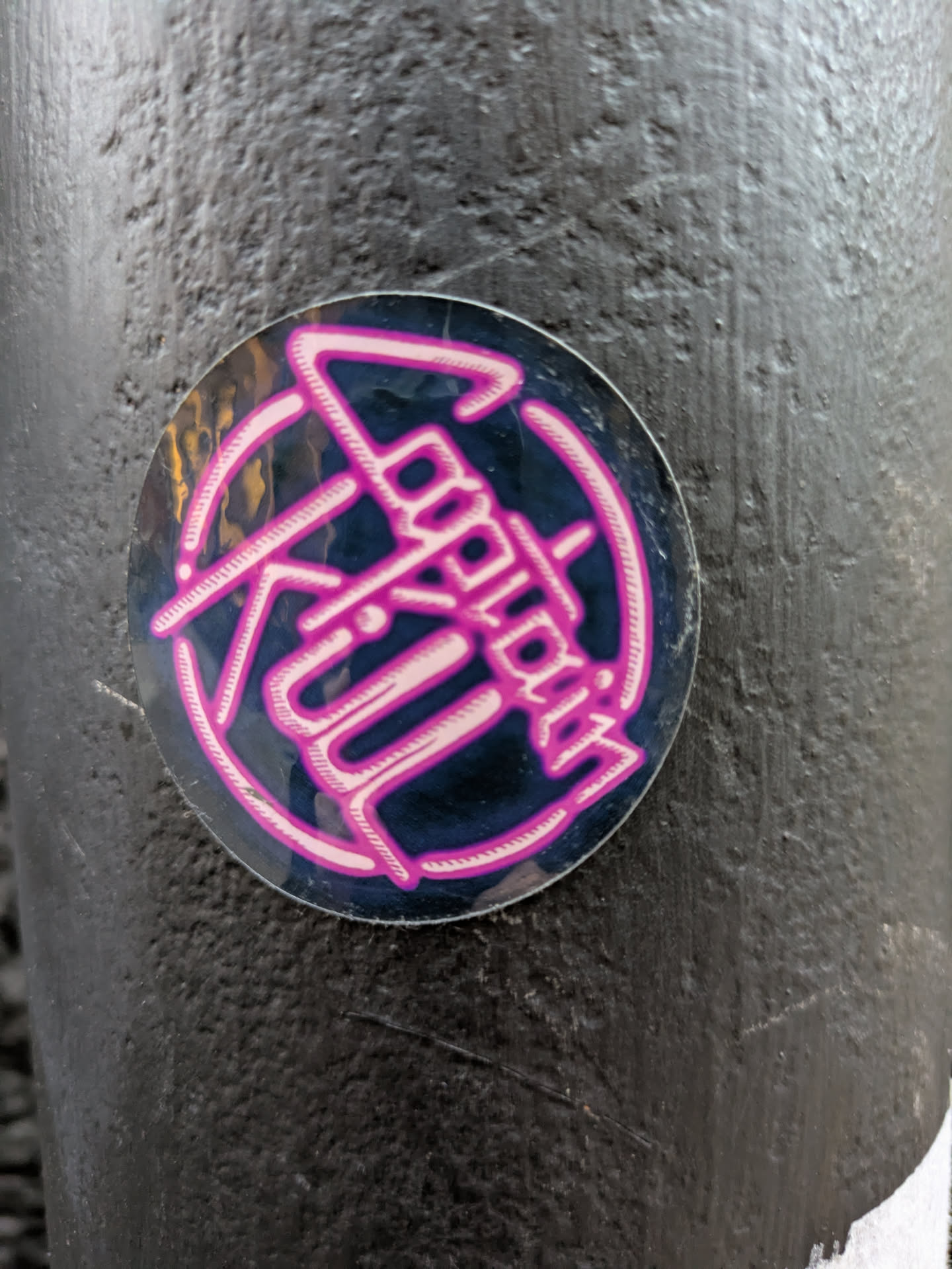 Round sticker with a dark background and pink logo. The logo appears to say "Logokill" in a stylized font. 