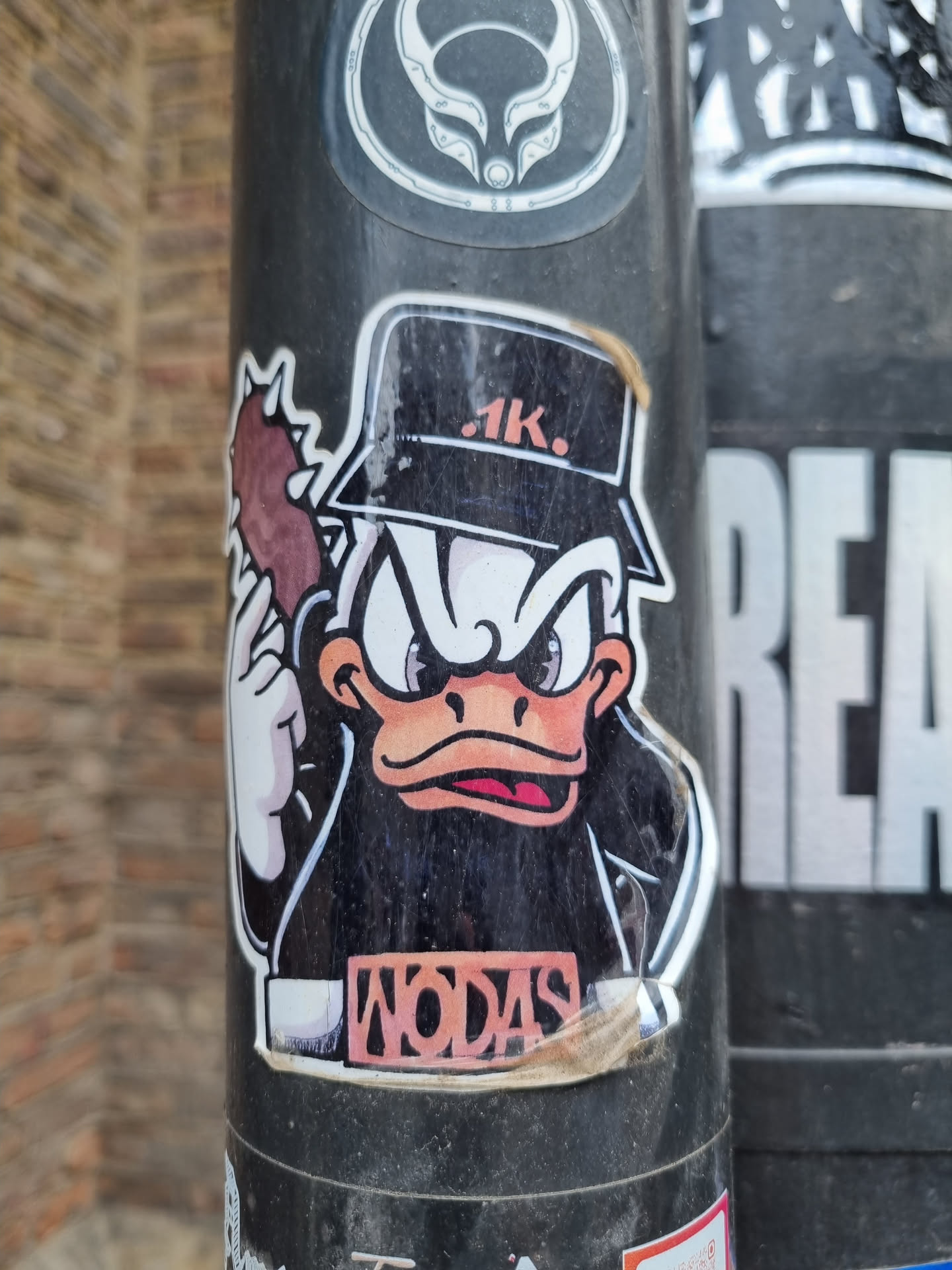 A sticker featuring a cartoon duck wearing a cap and a leather jacket, holding what looks like a club. The duck has an angry expression. The text \"WODAS\" is visible on its jacket. The sticker is worn and slightly damaged around the edges. 