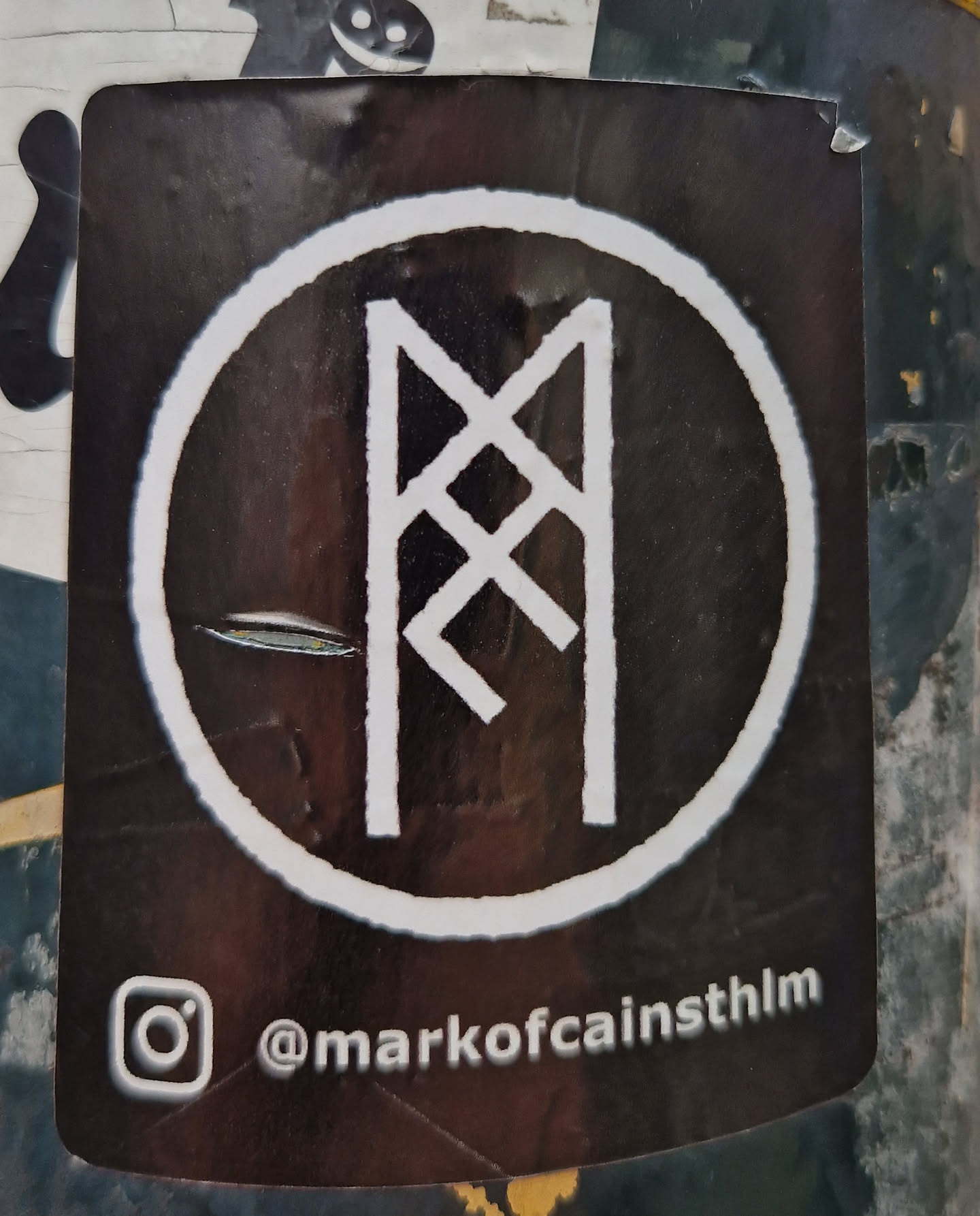 A round black and white sticker with a white rune symbol in the center. The Instagram handle @markofcainsthlm is visible at the bottom of the sticker.