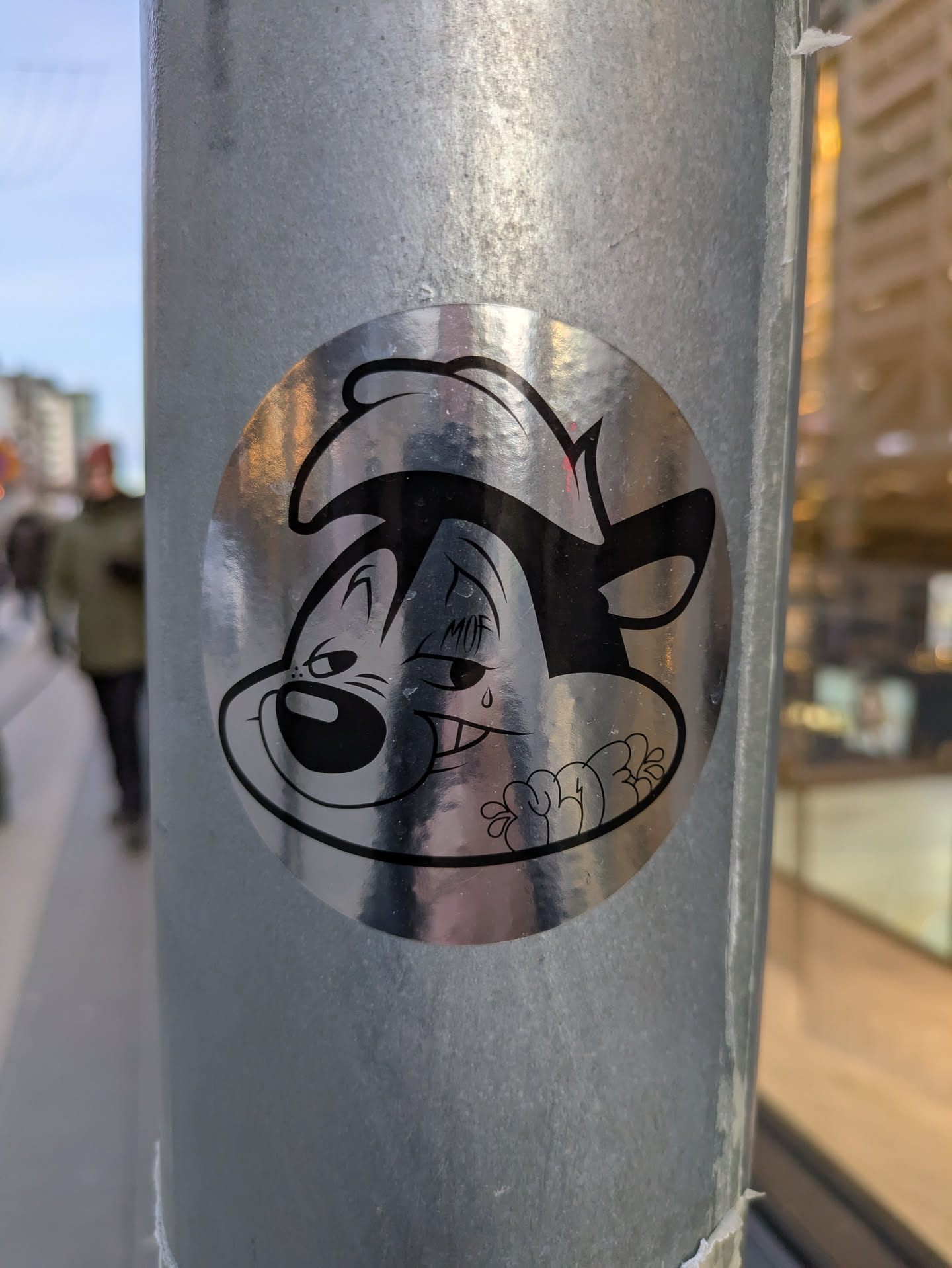 A silver, circular sticker featuring a stylized illustration of Pepe Le Pew, the Looney Tunes skunk. The design is in black and white with some added shading to create depth. Pepe is depicted with a mischievous expression.  The sticker appears to be made of a reflective material.
