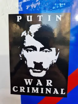 Black and white sticker depicting Vladimir Putin with the text 'PUTIN' above his image and 'WAR CRIMINAL' below.