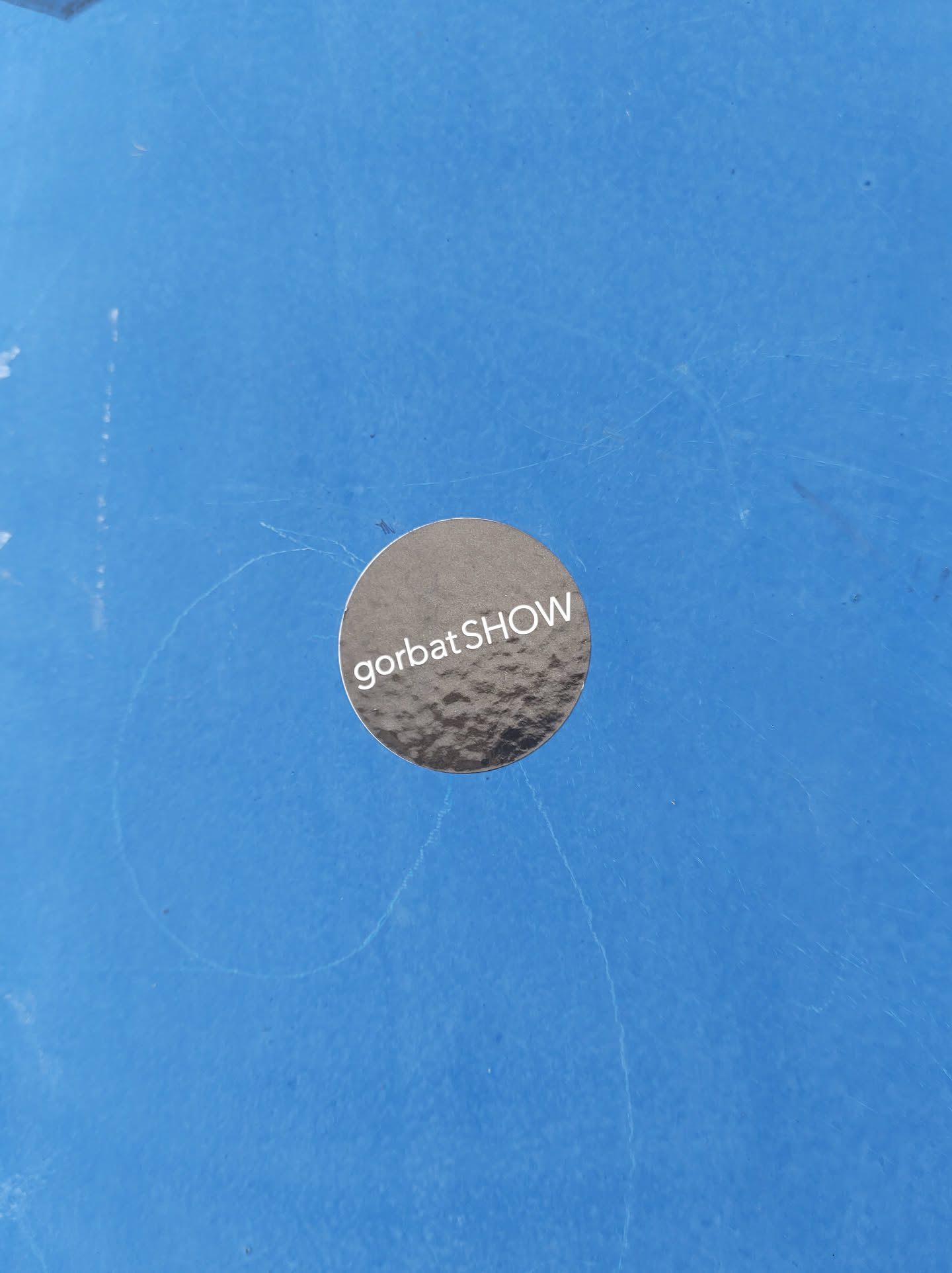 A round, metallic silver sticker with the text "gorbatSHOW" in white on a blue surface.