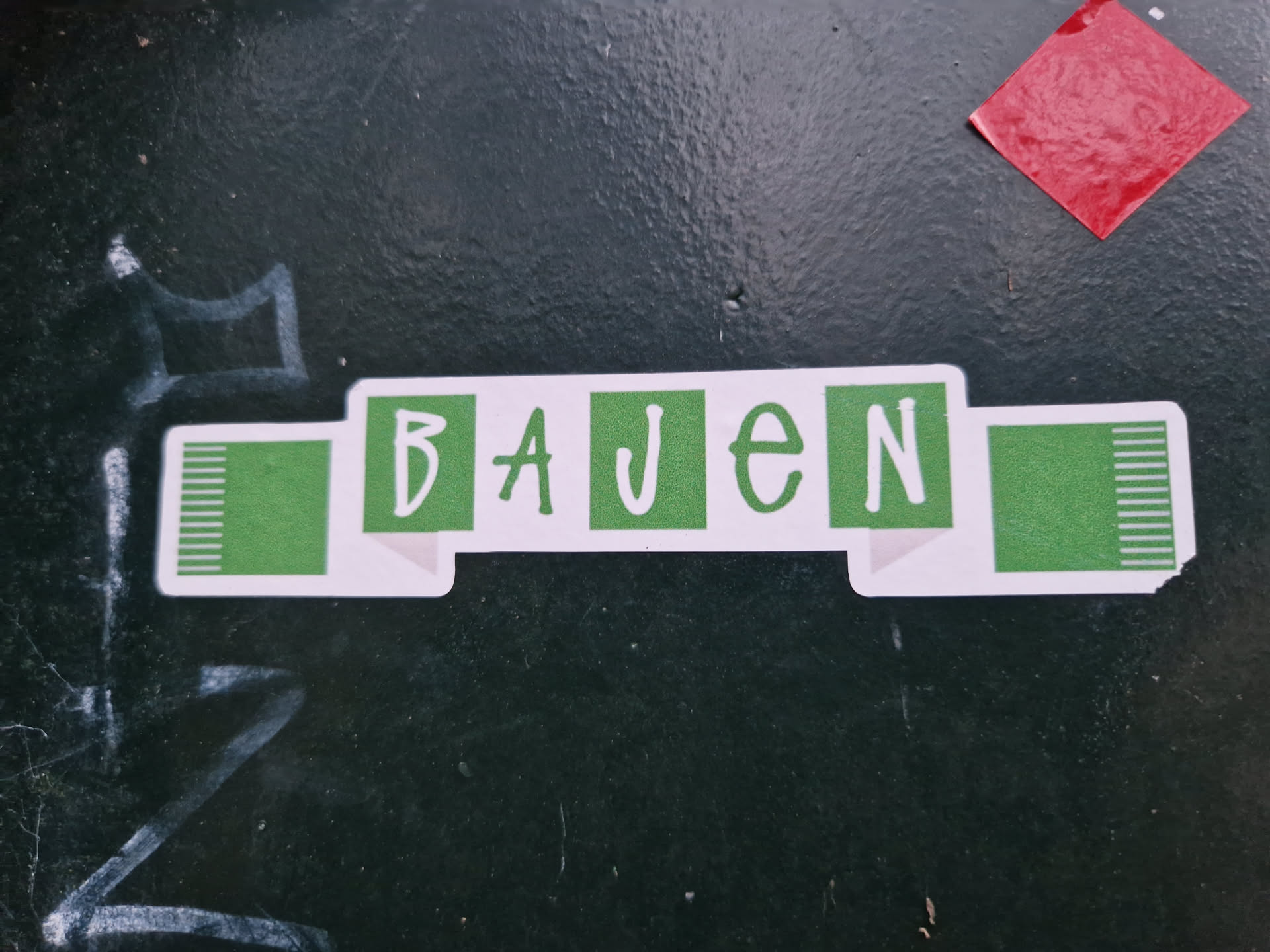 A sticker featuring the German word 'BAUEN' (meaning 'to build') in a simple, stylized design. The text is white against a green background and looks like a banner.  The green end pieces have white vertical lines. 