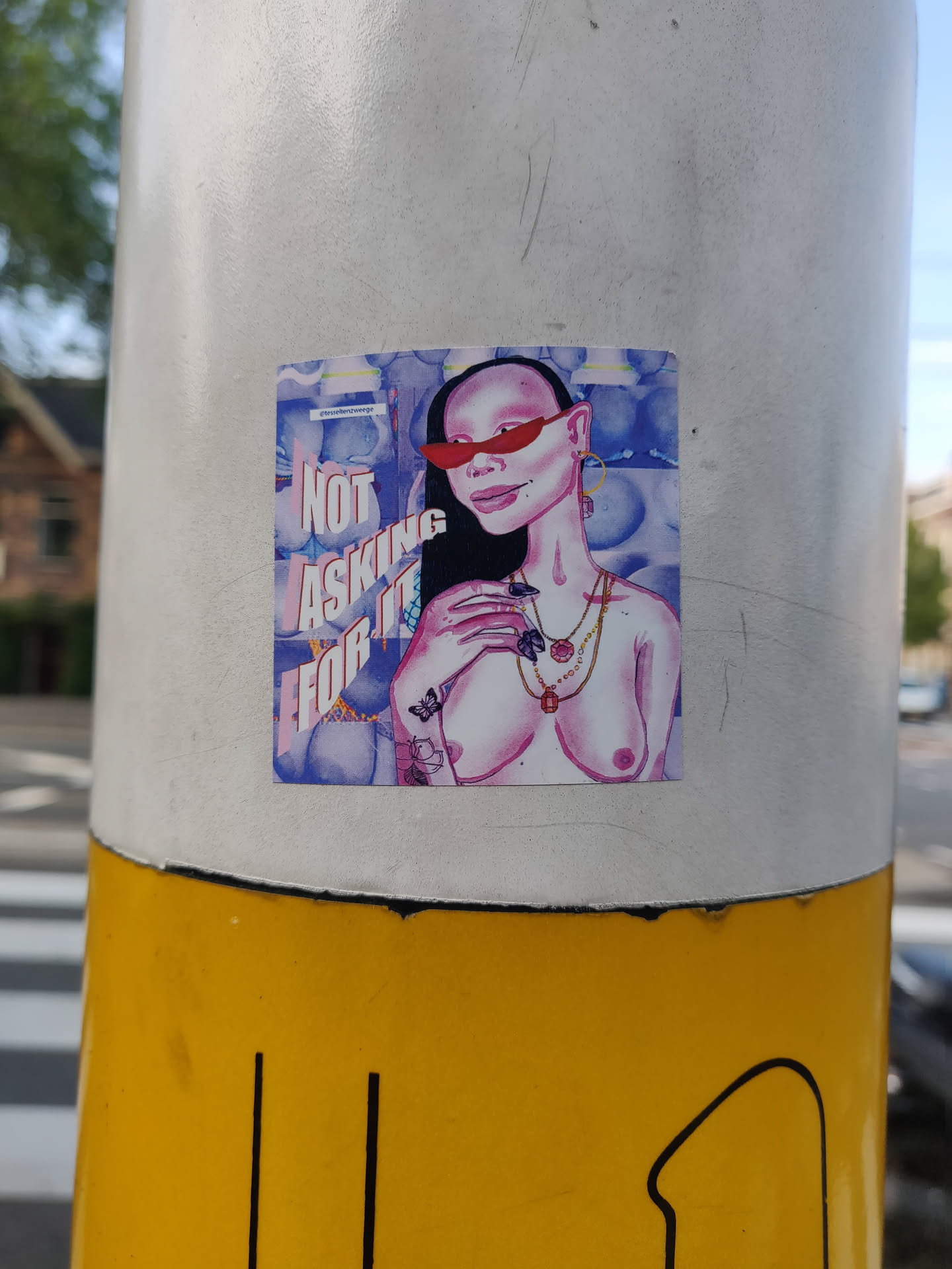 Sticker featuring an illustration of a topless woman with red sunglasses and jewelry. The background is a watercolor-like purple and blue design. The text 'Not asking for it' is prominently displayed on the sticker.