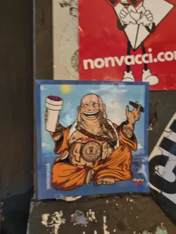 Sticker featuring a cartoon illustration of a Buddha figure with tattoos, holding a cigar and a purple drink. The sticker has a blue background and includes the Instagram handle @youngmone.