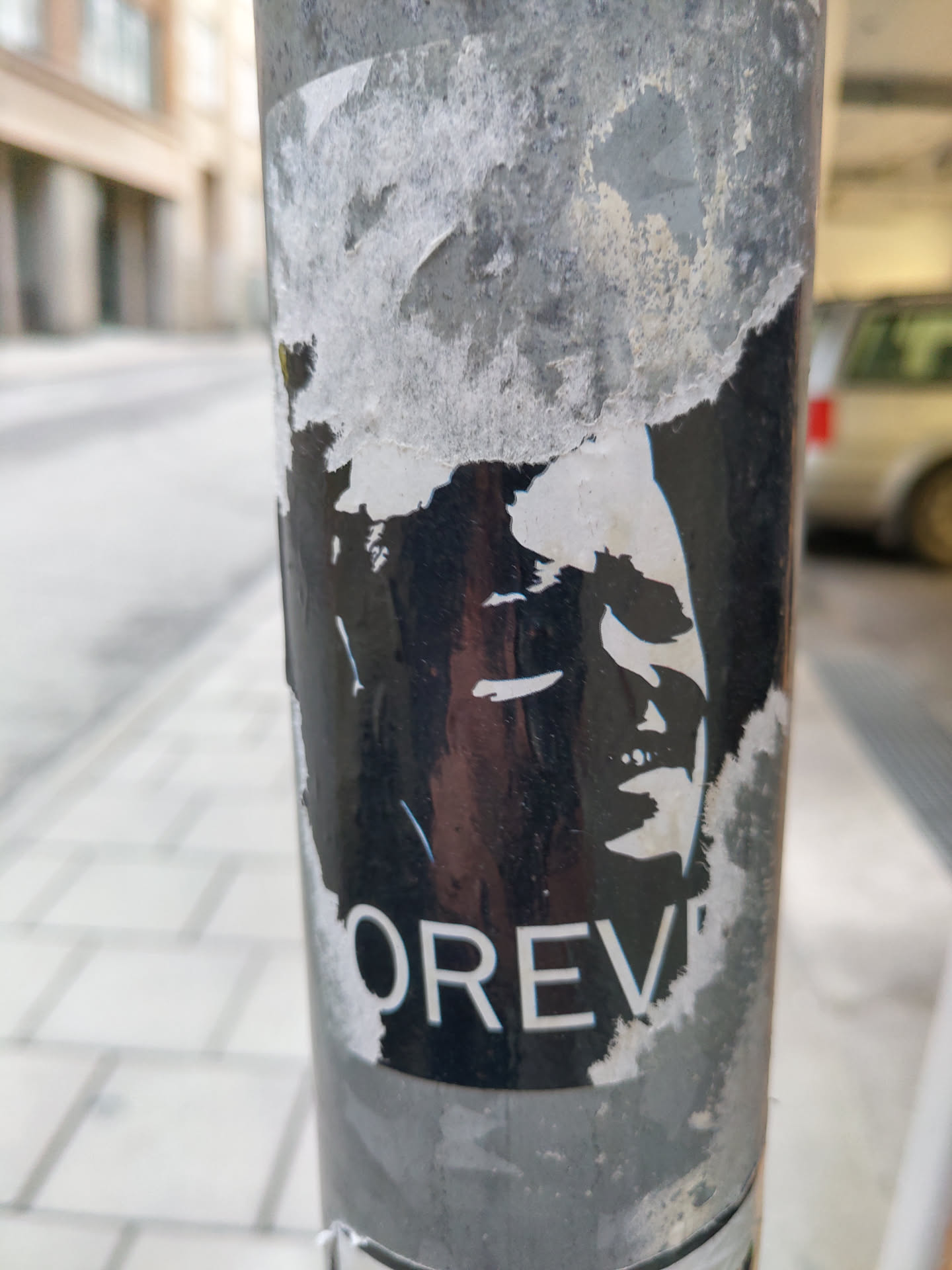 A black and white sticker with a portrait and the word "FOREVER" at the bottom. The sticker is partially damaged and peeled off.