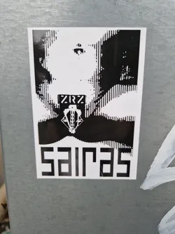A black and white sticker with a distorted face image and the word SAIRAS written in a bold, blocky font at the bottom.  There's also smaller text that reads ZRZ and a small graphic above SAIRAS. The style is reminiscent of glitch art or distorted imagery.