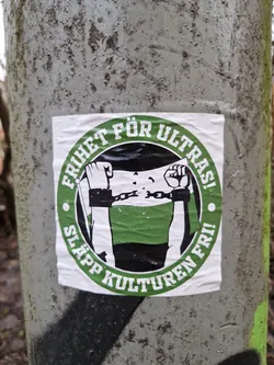 A sticker depicting a person with their hands cuffed behind their back, with the text "Frihet för ultras! Släpp kulturen fri!" which translates to "Freedom for ultras! Release the culture!" in Swedish. The sticker is round with green text and a black and white image.