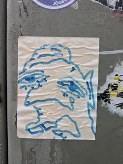 A sticker with a blue line drawing of a face. The drawing is simple and slightly abstract. The sticker is crumpled, giving it a textured look.