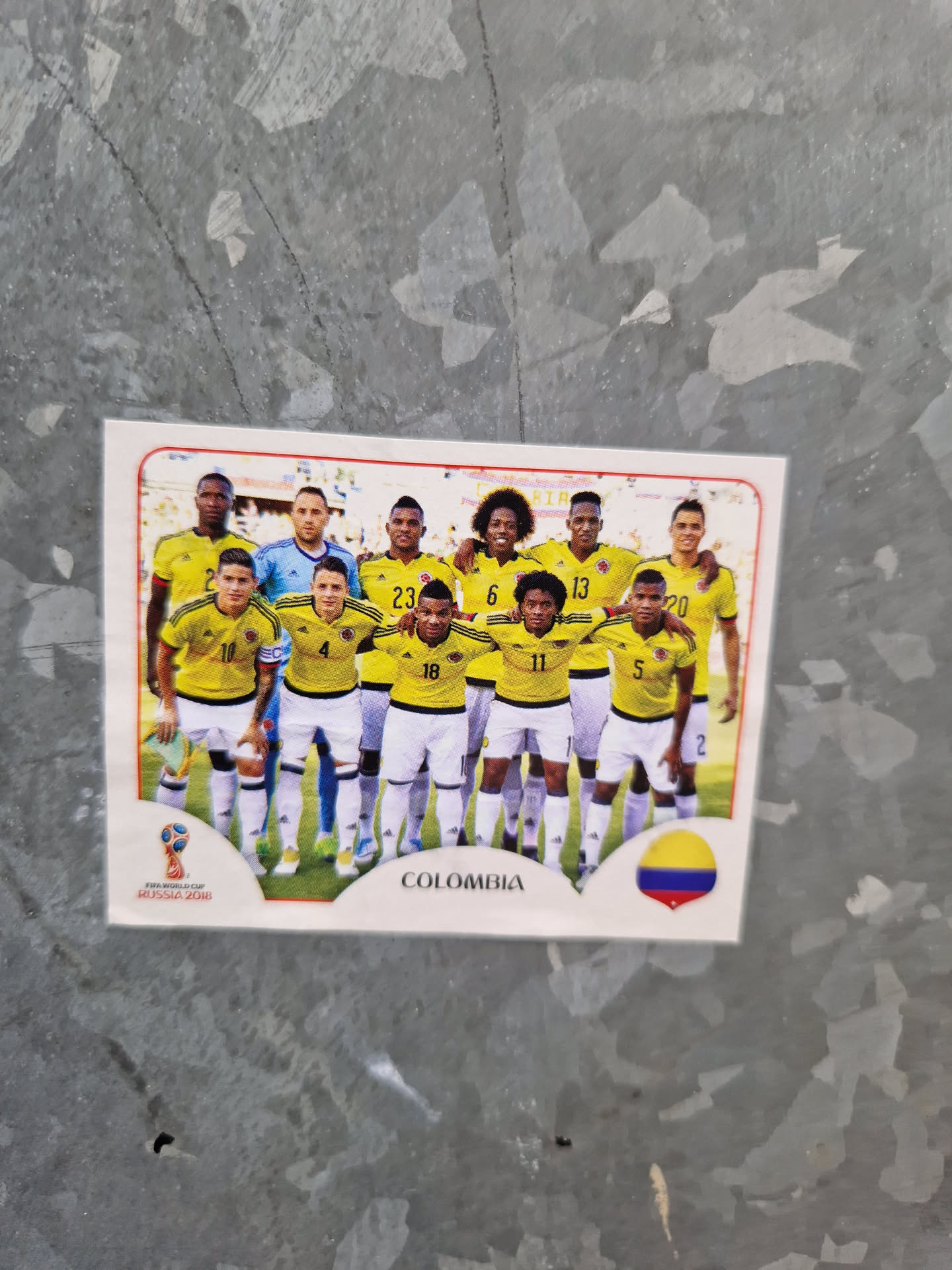 A sticker featuring the Colombian national football team. The players are wearing their yellow and blue uniforms.  The sticker includes the team name and the Colombian flag.